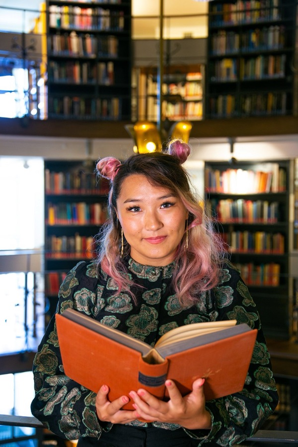 Yanjaa holding an open book in a library